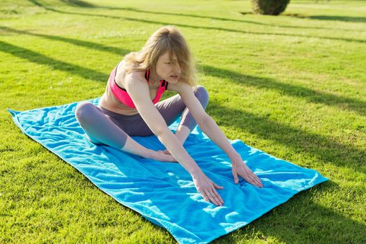 Middle-aged active woman doing sports exercises on a rug on the grass, in the morning. Healthy lifestyle, healthy body, people 40s age concept