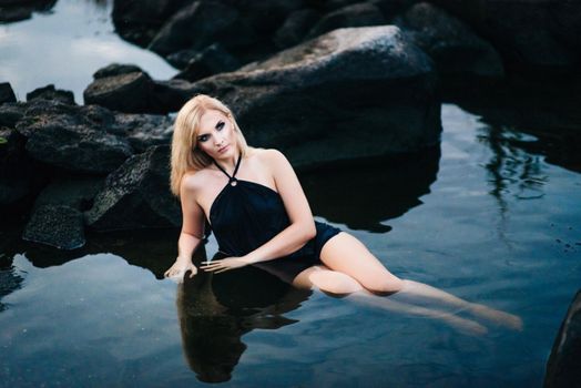 blonde girl in a black dress with blue eyes on the stone coast of the river