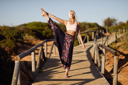 Woman enjoying the sunset on a beautiful beach in Cadiz, Andalusia, Spain. Caucasian female practicing yoga on wooden bridge.