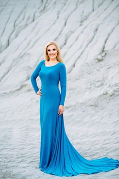 blonde girl in a blue dress with blue eyes in a granite quarry against the background of gravel