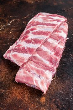 Rack of raw pork spare ribs on butcher table. Dark background. Top view.