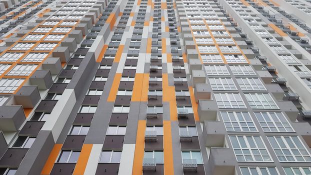 Bottom view of the facade of a new multi-storey residential building with balconies and gray and orange windows.