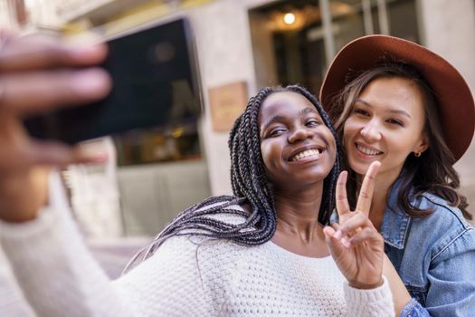 Two multiethnic women making selfie and grimacing with a smartphone.