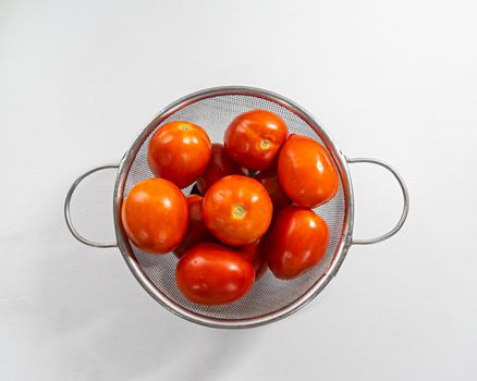 Close up image of Fresh red tomatoes washed with water and kept in a net pot with plain white background.