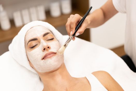 Aesthetics applying a mask to the face of a Middle-aged woman in modern wellness center. Beauty and Aesthetic concepts.