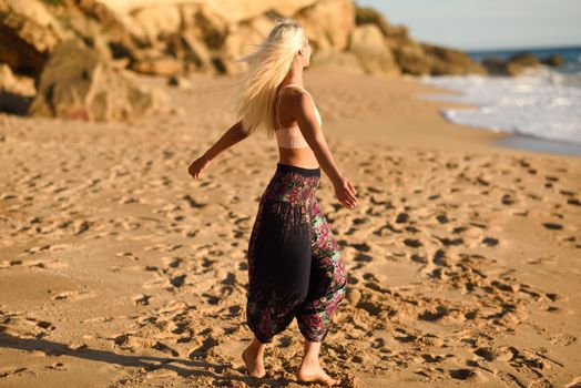 Woman doing yoga at sunset on a beautiful beach in Cadiz, Andalusia, Spain. Young female opening arms and breathing the sea air.