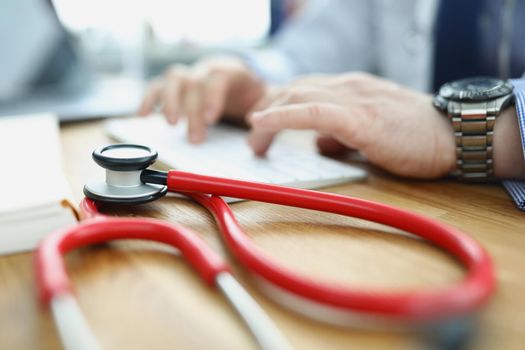 Close-up of medical equipment red stethoscope on workplace. Doctor typing on keyboard, medical building for health checkup. Medicine, clinic, appointment, healthcare concept