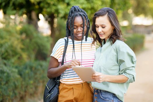 Two multiethnic women consulting something on a digital tablet outdoors.