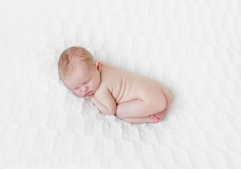 Adorable hairy naked infant sleeping on his belly tighly, light skin and cute position