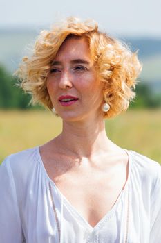 Beautiful blonde woman with short curly hair outdoors. Romantic model in summer white dress.