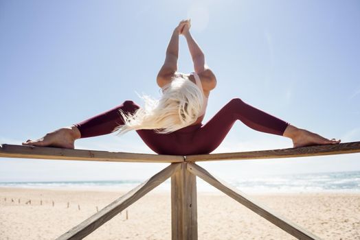 Caucasian woman practicing yoga at seashore. Young female on wooden bridge, Andalusia, Spain.