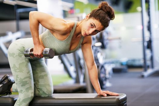 Caucasian strong woman lifting some weights and working on her triceps and biceps in a gym with dumbbells.