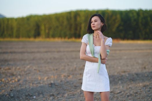 Pretty young Asian woman, walking in the countryside, wearing a white dress.