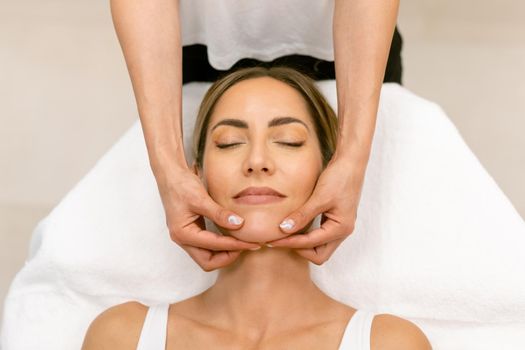 Middle-aged woman having a head massage in a beauty salon. Body care treatment in a beauty centre.