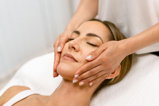 Middle-aged woman having a head massage in a beauty salon. Body care treatment in a beauty centre.