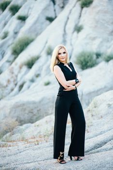 blonde girl in a black trouser suit with blue eyes on the background of a granite quarry from gray rubble