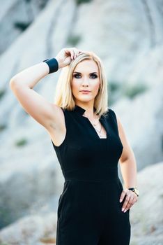 blonde girl in a black trouser suit with blue eyes on the background of a granite quarry from gray rubble