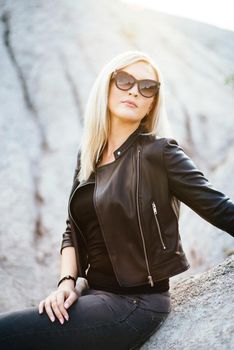 blonde girl in a black trouser suit with blue eyes on the background of a granite quarry from gray rubble