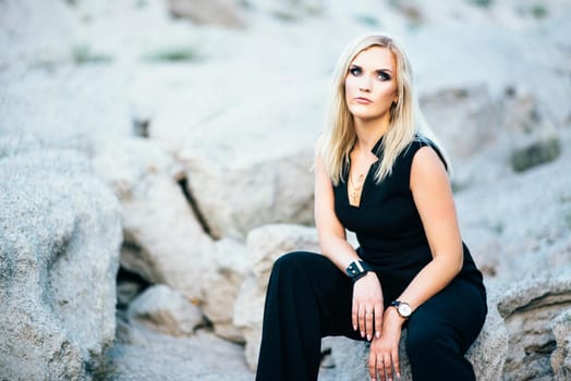 blonde girl in a black trouser suit with blue eyes on the background of a granite quarry from gray rubble