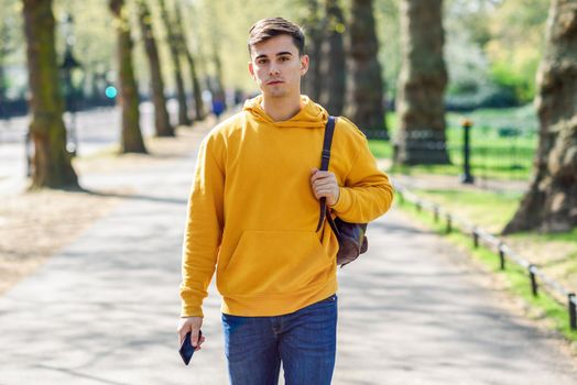 Young urban man using smartphone walking in street in an urban park in London, UK.