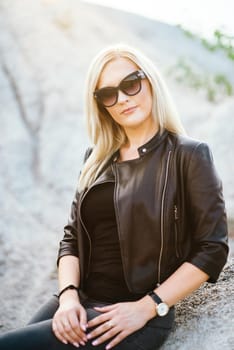 blonde girl in a black trouser suit with blue eyes on the background of a granite quarry from gray rubble