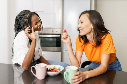 Two friends having a healthy snack while chatting at home. Multiethnic women.