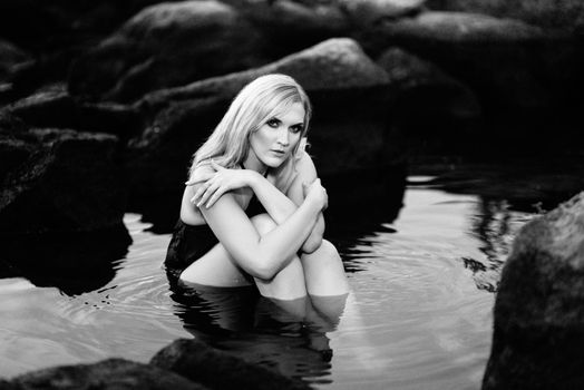 blonde girl in a black dress with blue eyes on the stone coast of the river