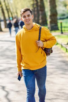 Young urban man using smartphone walking in street in an urban park in London, UK.