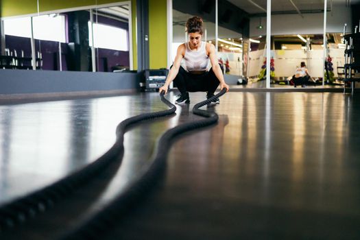 Young and athletic woman using training ropes in a gym. Fitness concept.