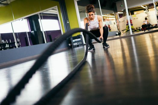 Young and athletic woman using training ropes in a gym. Fitness concept.