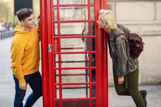 Young happy couple of friends near a classic British red phone booth