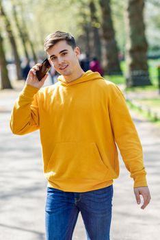 Young urban man using smartphone walking in street in an urban park in London, UK.