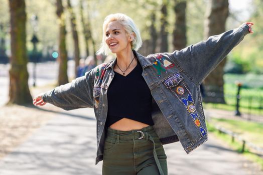 Young woman arms raised enjoying the fresh air in green urban park in London.