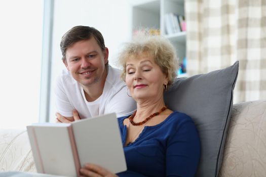 Portrait of senior woman and middle aged man reading book. Mother and son smiling spending time together on weekend. Family, leisure, education, home, hobby concept