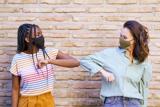 Multiethnic young women wearing masks greeting at each other with their elbows outdoors