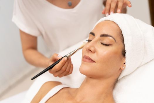 Aesthetics applying a mask to the face of a Middle-aged woman in modern wellness center. Beauty and Aesthetic concepts.