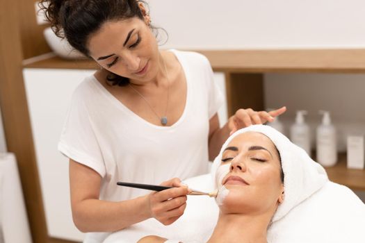 Aesthetics applying a mask to the face of a Middle-aged woman in modern wellness center. Beauty and Aesthetic concepts.