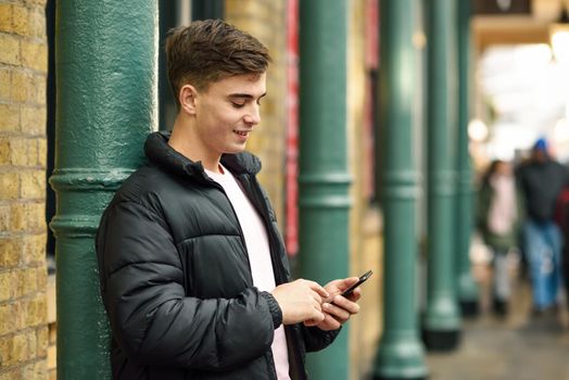 Young urban man using smartphone in urban background in London, UK