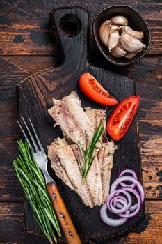 Smoked Sardine fish fillet on wooden board with herbs. Dark wooden background. Top view.