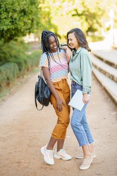 Two multiethnic girls posing together with colorful casual clothing outdoors.