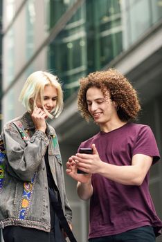 Happy couple using smartphone in urban background. Young man and woman wearing casual clothes in a London street.