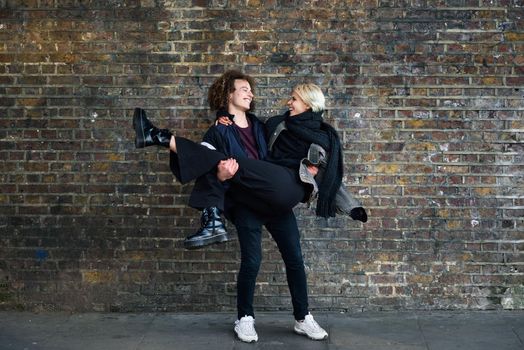 Man holding his girlfriend in his arms. Young couple enjoying Camden town in front of a brick wall typical of London, UK