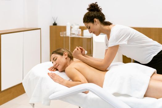 Female masseuse giving a back massage to a woman in a beauty parlour. Body care treatment in a beauty centre.