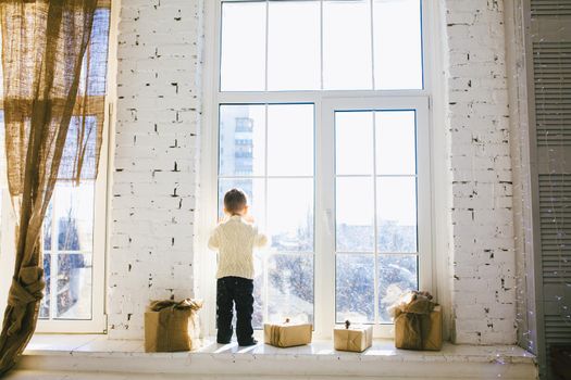 Christmas concept. Theme Christmas morning. Dreaming boy in anticipation of a miracle on a Christmas. baby look out window for the winter Christmas.