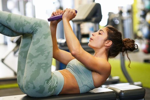 Sporty young female, wearing sportswear, on yoga mat doing situps with plate weights in gym. Fitness woman doing abs crunches.