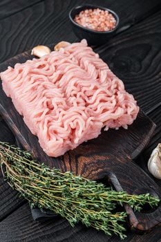 Fresh Raw mince or ground chicken meat on wooden chopping board with thyme. Black wooden background. Top view.