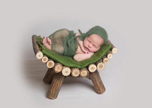 Cute sleeping baby wrapped in green diaper and knitted hat on small wooden crib.