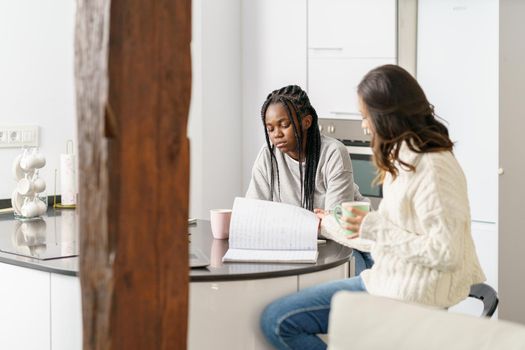 Two college girls studying together at home while drinking coffee. Multiethnic women.