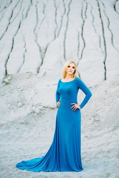 blonde girl in a blue dress with blue eyes in a granite quarry against the background of gravel