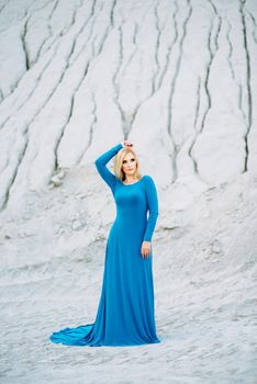 blonde girl in a blue dress with blue eyes in a granite quarry against the background of gravel